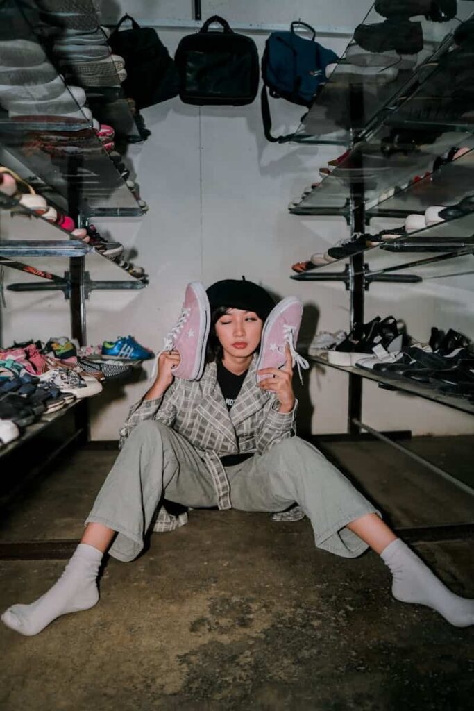 A young woman sits on the floor of a shoe store holding sneakers in a trendy and casual pose.