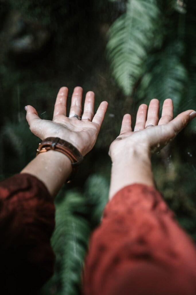 Close-up of hands under rain outdoors, embracing nature's touch.