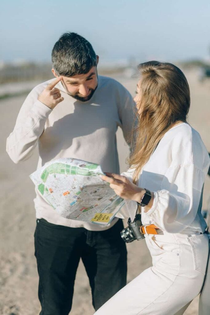 A man and woman study a map outdoors, planning travel directions on a sunny day.