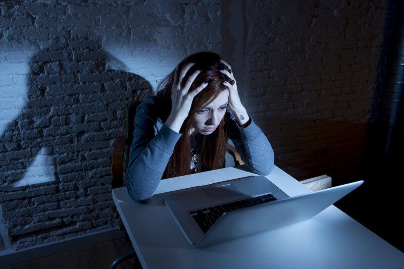 A young person sits solemnly at a dimly lit desk, surrounded by digital messages of online harassment