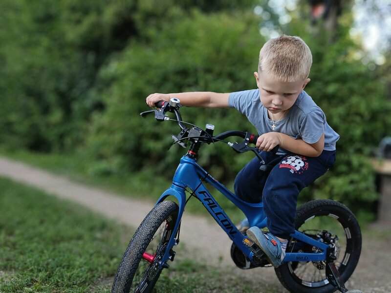 A young boy riding a blue bike down a dirt road