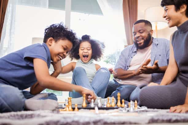 Funny african american children playing chess with mom and dad at home
